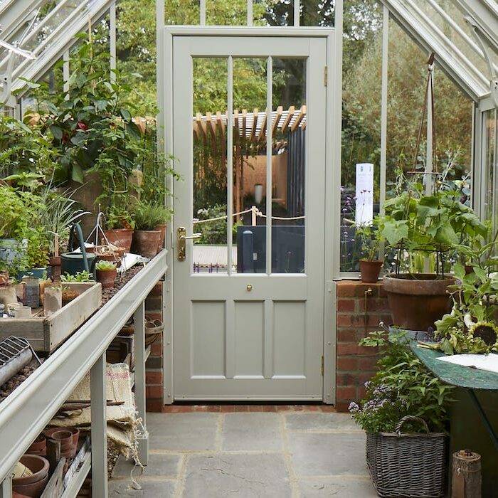 white greenhouse with grey paving and plants either side